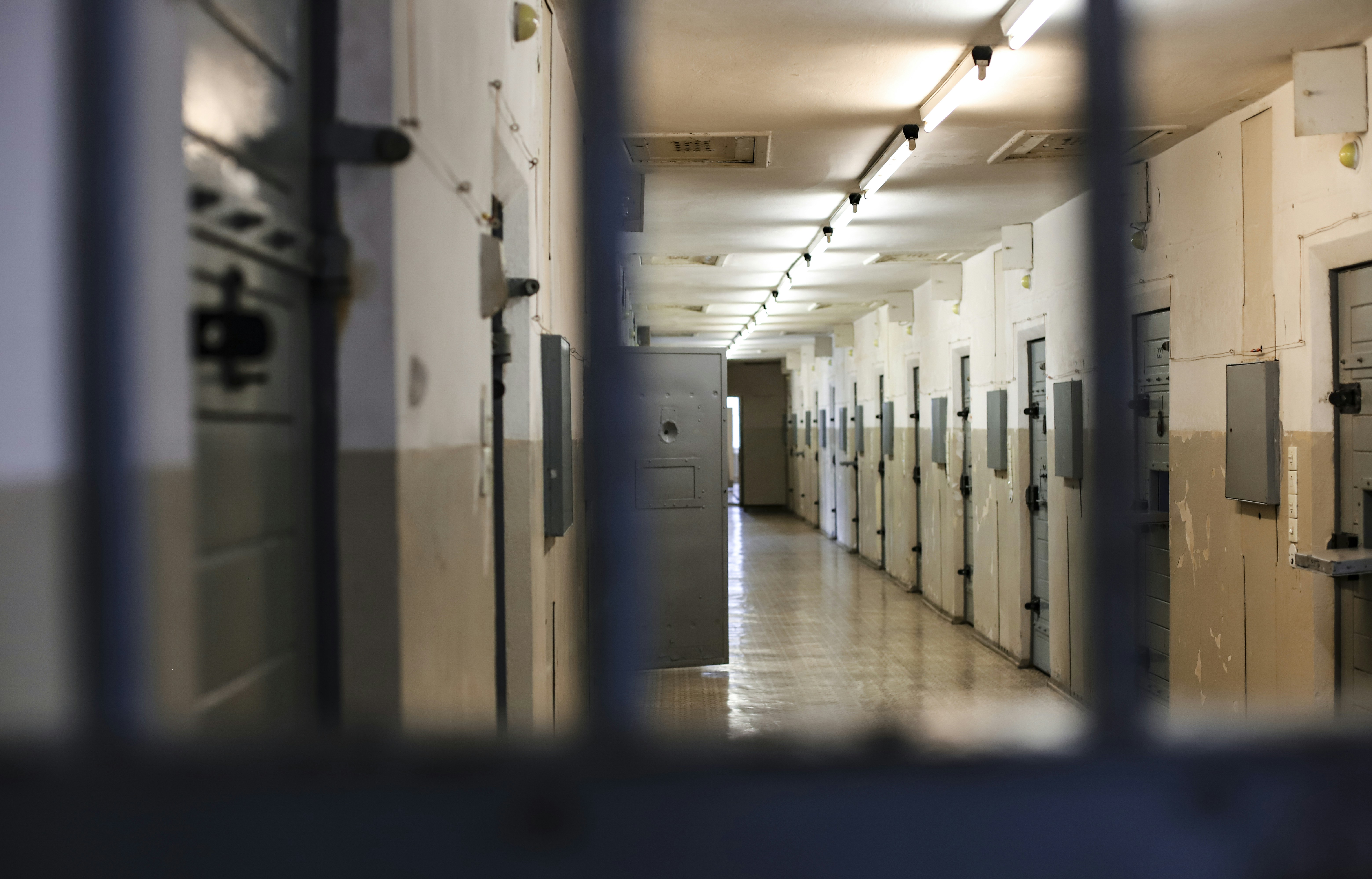 An inmate behind bars looks down an emtpy, long hallway in a jail.